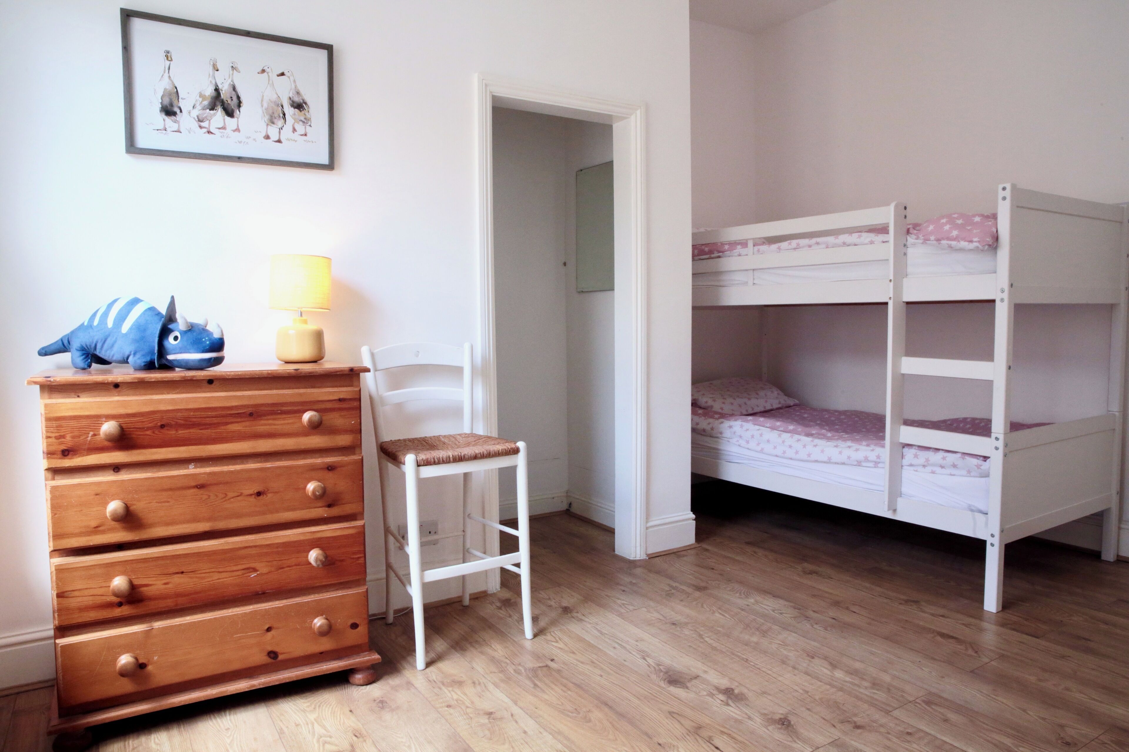 A child's room with a bunk bed, wooden dresser, chair, and a lamp.