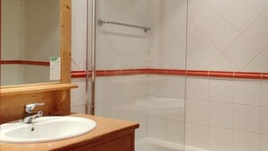 Un baño con tocador de madera, un espejo grande, un lavabo blanco, cabina de ducha con vidrio y una bañera blanca.