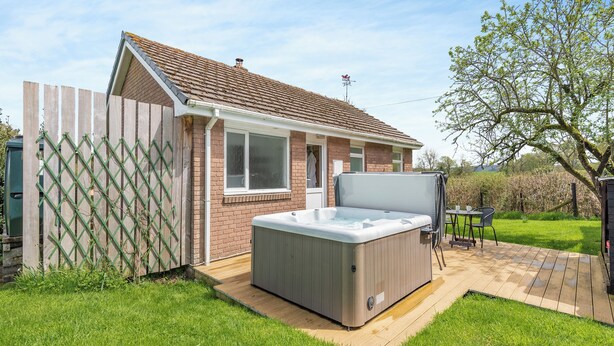 Een woonhuis met een bakstenen gevel, een houten terras en een jacuzzi.