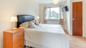 Een slaapkamer met een bed, nachtkastjes, een lamp, een stoel, een televisie en een deur.