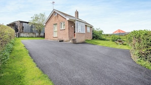Een gelijkvloers huis met een verharde oprit en een gazon.