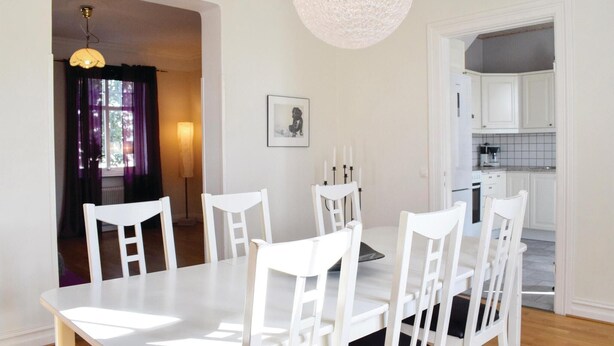 Un coin repas avec une table et des chaises blanches, un lustre et un tableau encadré au mur.