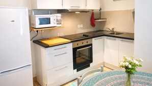 A compact kitchen with a microwave, oven, and sink. There is a wooden cutting board and a red towel hanging above the stove. - The waves of money - Le Lavandou (LE LAVANDOU)