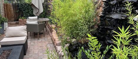 A patio area with a stone pathway, outdoor furniture, and a small waterfall feature.