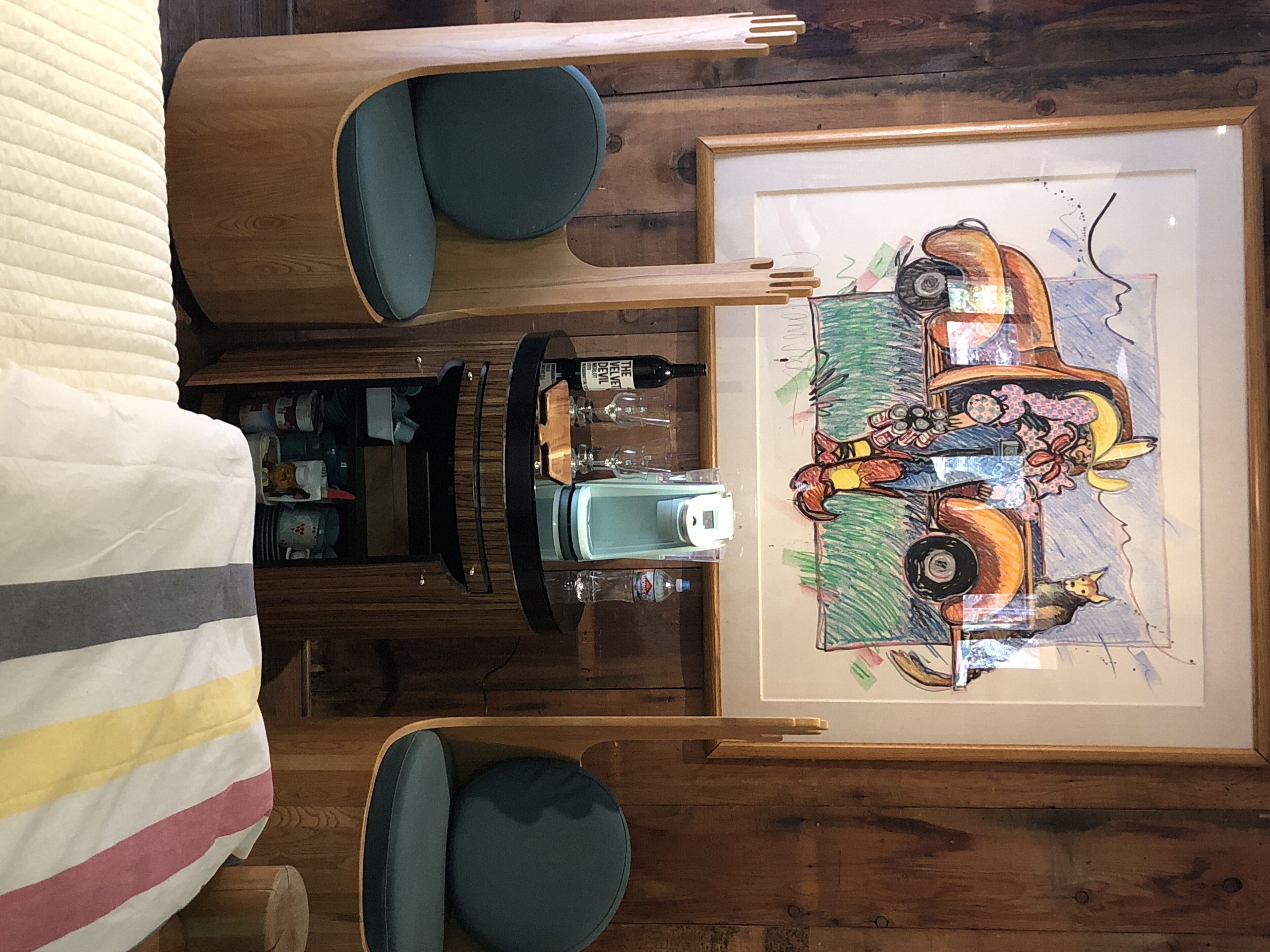 A room with a bed, a wooden dresser, a framed artwork, and a small table with a camera and wine glasses.