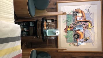 A room with a bed, a wooden dresser, a framed artwork, and a small table with a camera and wine glasses.