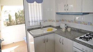 Een keuken met witte kastjes, een granieten aanrecht, een gasfornuis en een raam met een blauw gordijn.