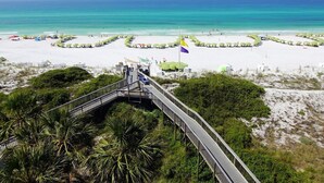 A beach with a wooden boardwalk leading to a white sandy area with umbrellas and lounge chairs.
