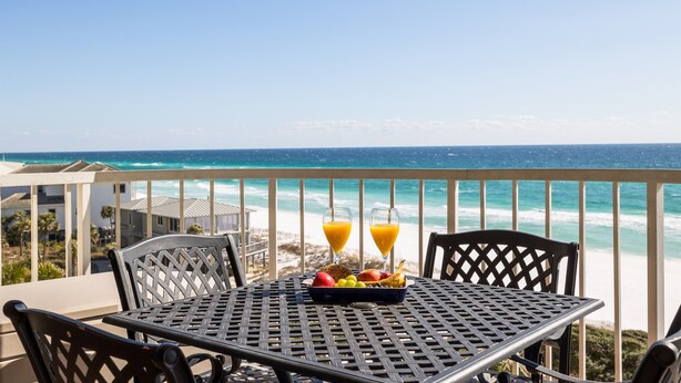 A balcony with a table set for two, overlooking a beach and ocean.