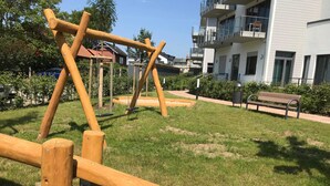A playground with swings and a bench in a grassy area with buildings in the background. - Haffduurn, Germany (Glowe)