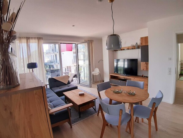 A modern living room with a sofa, dining table, chairs, and a TV.