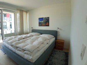 A bedroom with a large bed, a nightstand, a painting on the wall, and a window with curtains.