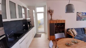 A modern kitchen with white cabinets, a black countertop, and a dining area with a wooden table and chairs. - Haffduurn, Germany (Glowe)