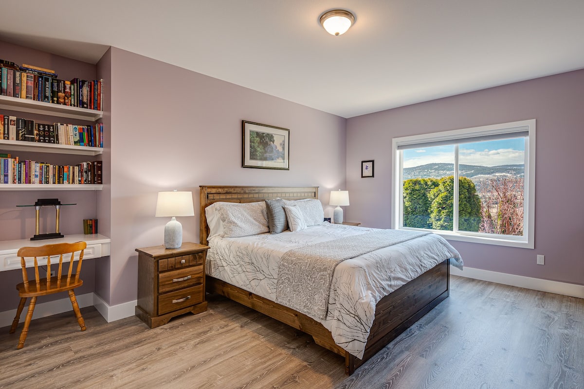 Une chambre à coucher avec un grand lit, un bureau avec des étagères, une chaise et une fenêtre donnant sur un beau paysage.