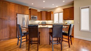 Una cocina con armarios de madera, un refrigerador de acero inoxidable, un microondas y una zona de comedor con cuatro sillas.