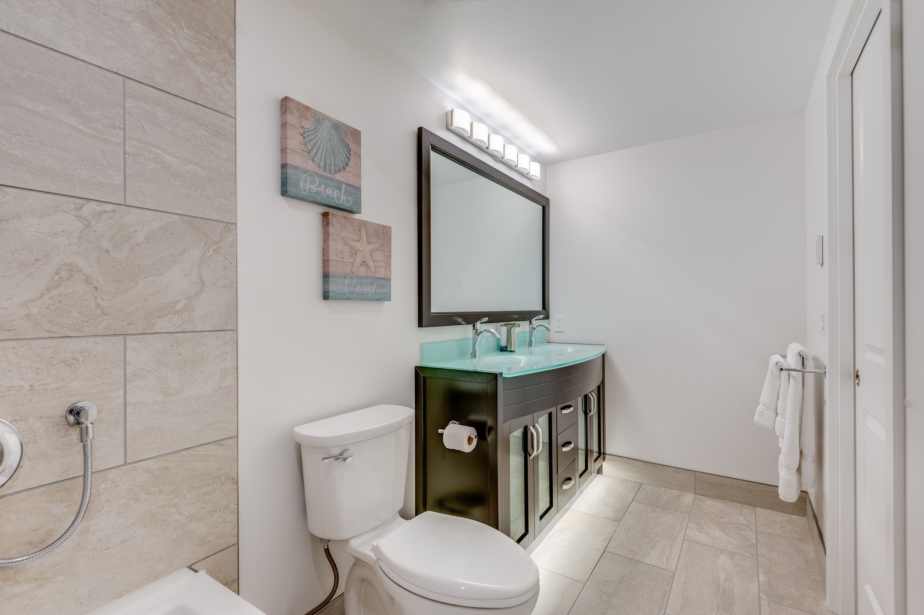 A modern bathroom with a toilet, sink, and shower. There are decorative wall art pieces and a mirror above the sink.