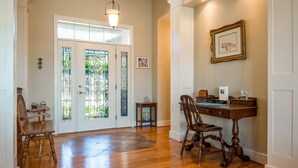 Una habitación con piso de madera, un escritorio con silla, una lámpara colgante y una puerta con paneles de vidrio.