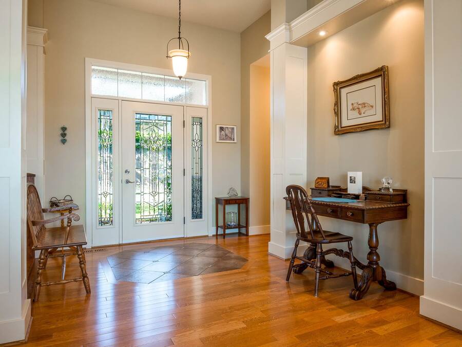 A room with a wooden floor, a desk with a chair, a hanging light fixture, and a door with glass panels.