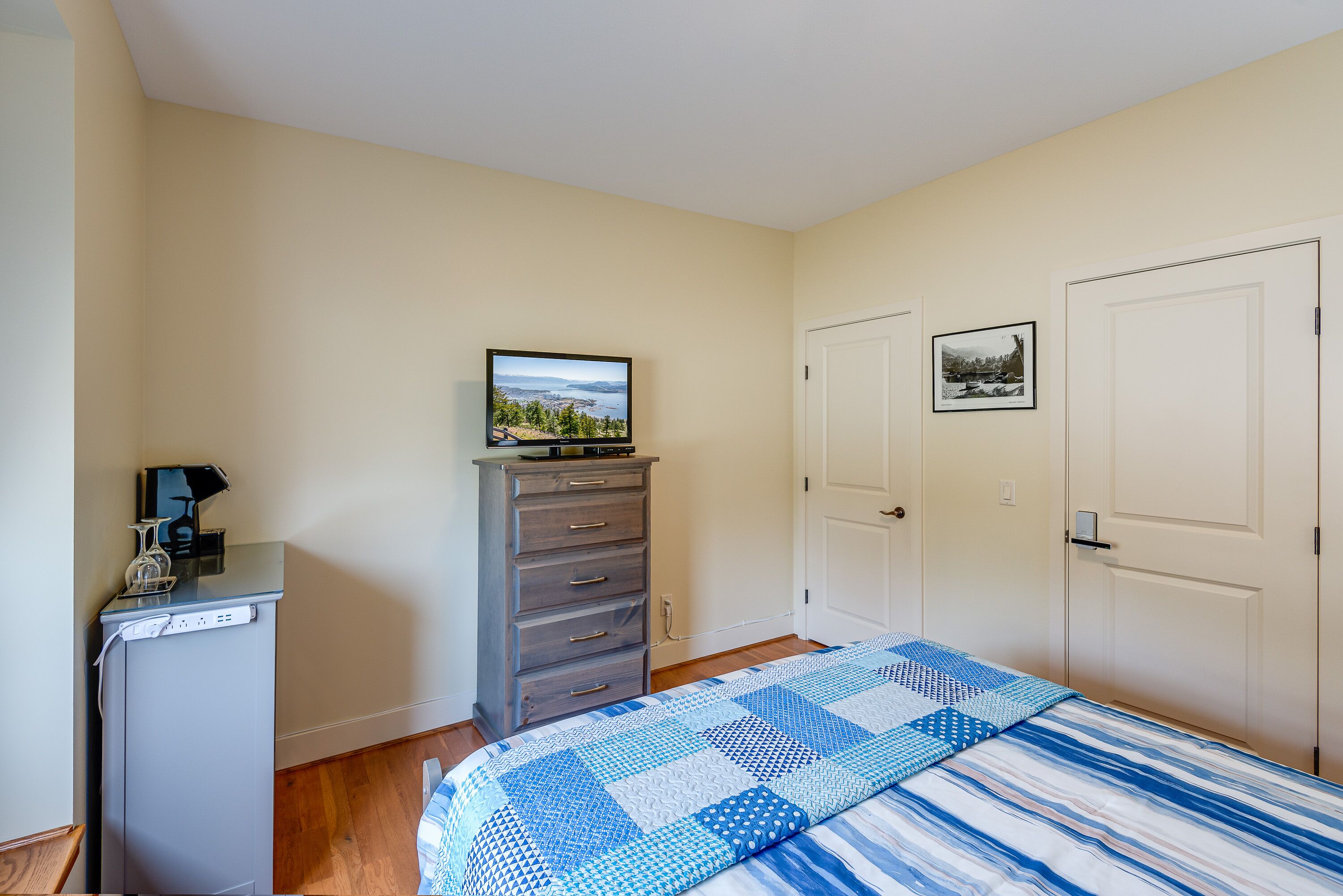 A bedroom with a bed, a dresser, a television, and two doors.