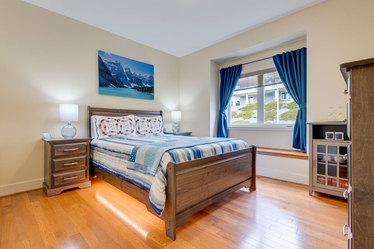 Une chambre à coucher avec un lit en bois, une table de chevet, une commode et une fenêtre avec des rideaux.