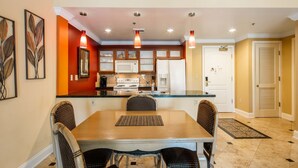 A dining area with a wooden table and four wicker chairs, a kitchen with white appliances, and a door with a sliding glass window. - Gorgeous condo, super comfy, with view of the pool in Lake Las Vegas Village. (Henderson)