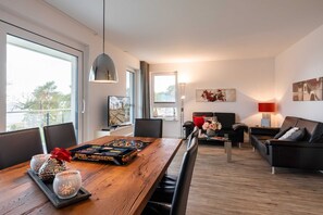 Un salon moderne avec une table à manger en bois, des canapés en cuir noir et une grande fenêtre laissant entrer la lumière naturelle.