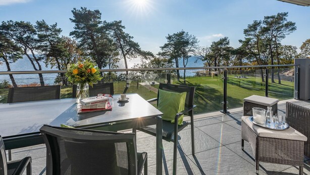 Een terras buiten met een tafel voor twee, uitkijkend op een wateroppervlak en een golfbaan.