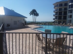 A pool area with lounge chairs and a building with a blue roof. - Beautifully redecorated 2 bedroom condo in quiet section of town (New Smyrna Beach)