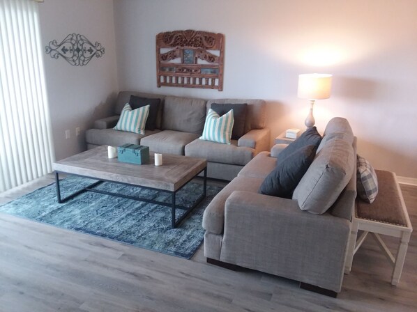 A living room with two sofas, a coffee table, and a lamp. - Beautifully redecorated 2 bedroom condo in quiet section of town (New Smyrna Beach)