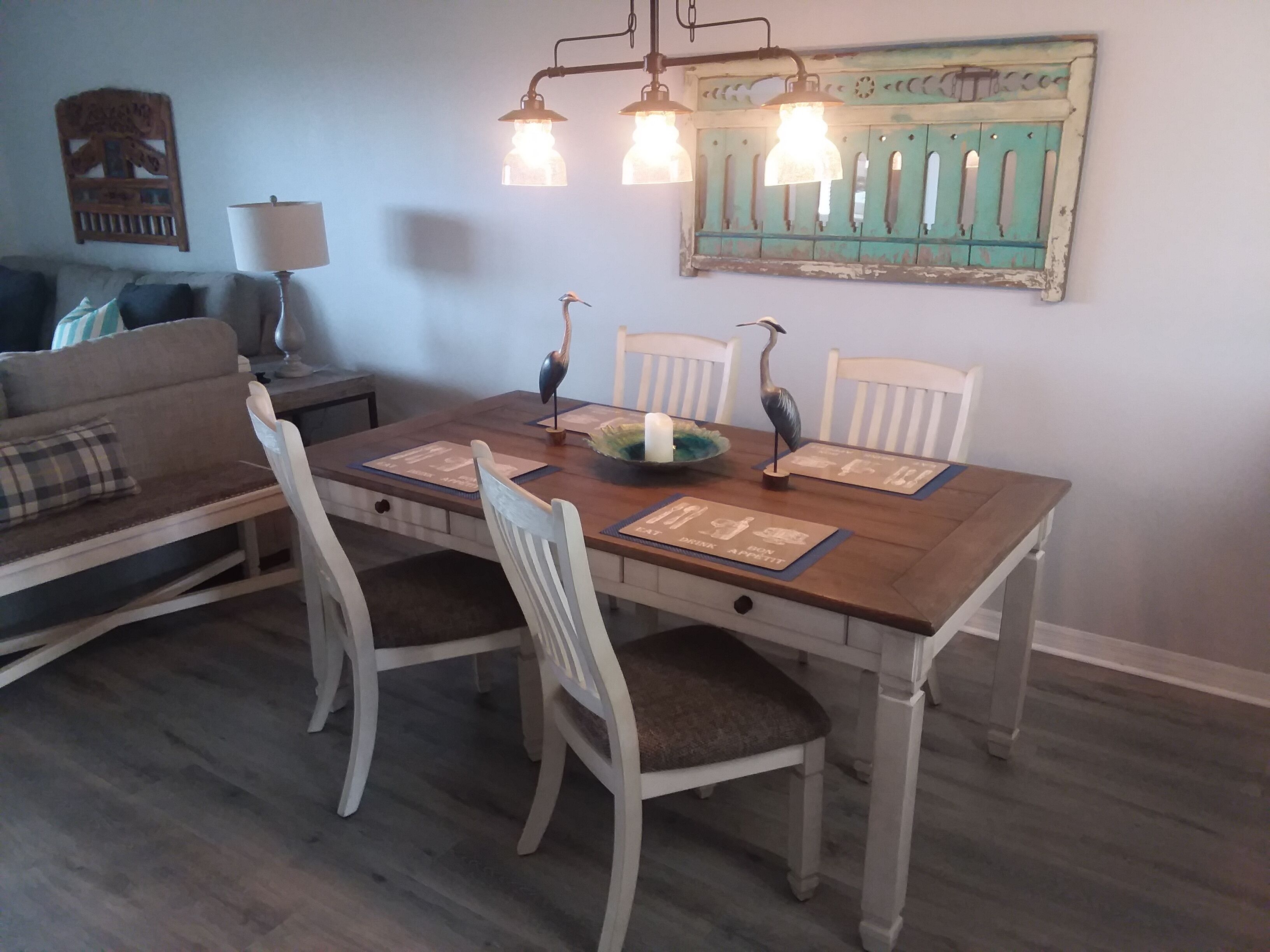 Una mesa de comedor con sillas blancas, un adorno en la pared y una lámpara a un lado.