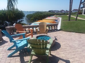 Relax in the outdoor seating area with Adirondack chairs surrounding a fire pit, overlooking a serene body of water.