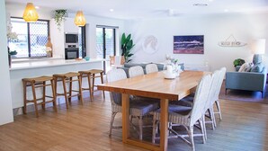 A modern kitchen with a dining area, wooden table, wicker chairs, and pendant lights. - Noosa Heads Endless Summer Beach Retreat (Noosa Heads)