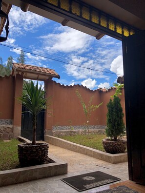A courtyard with a tiled floor, a palm tree, and a small coniferous tree in planters. - Illari Kusi (Urubamba)