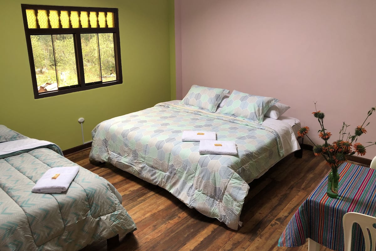 A room with a bed, a window, a table with a vase, and a chair.