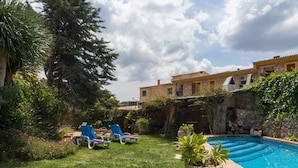 Uma área de piscina com piscina azul cristalina, duas espreguiçadeiras azuis e um gramado.