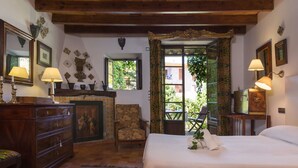 Um quarto acolhedor com teto de madeira, uma cama grande, uma cômoda e uma cadeira. Há uma janela com vista para o verde lá fora.
