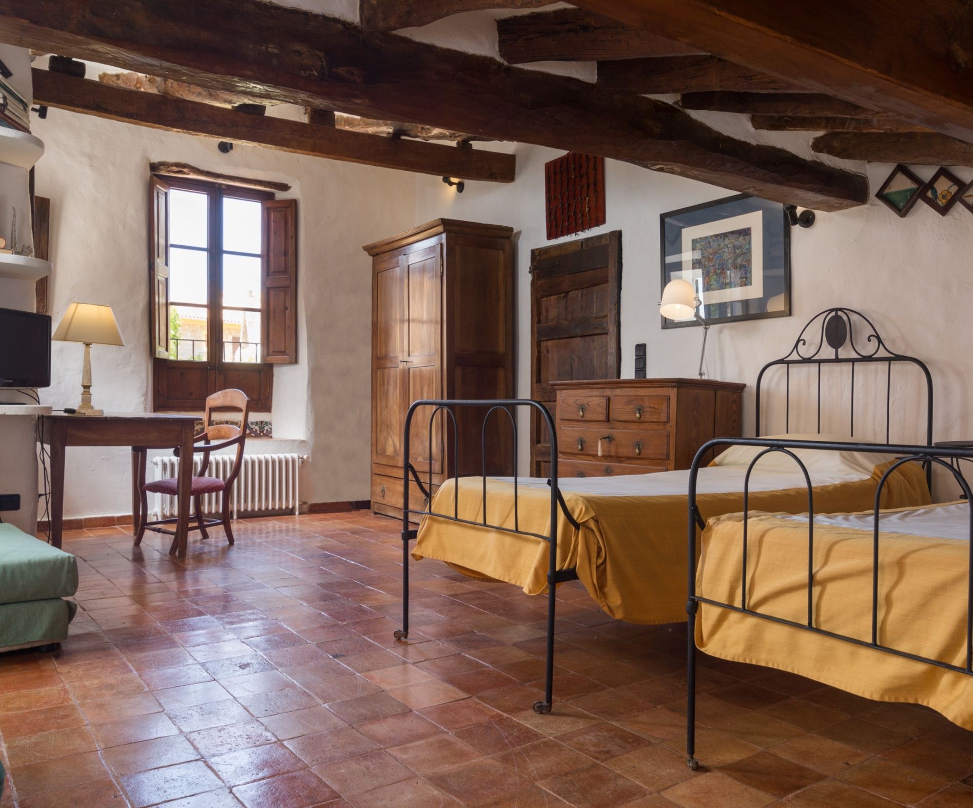 A room with two metal beds, a wooden cabinet, a wooden chair, a radiator, and a window.