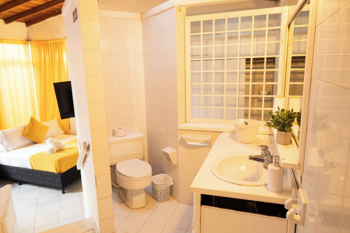 A hotel room with a bed, a bathroom with a sink, toilet, and a window with a grid pattern.