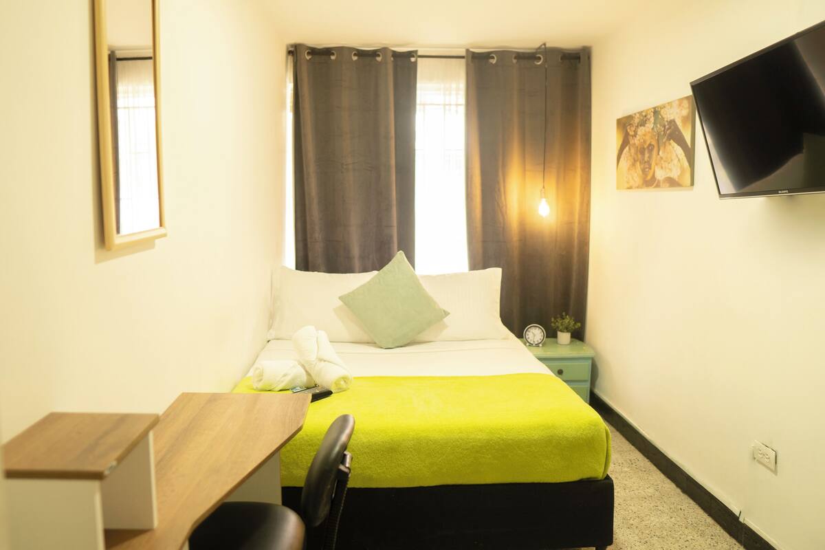 A hotel room with a bed, a desk, a chair, a television, and a window with curtains.