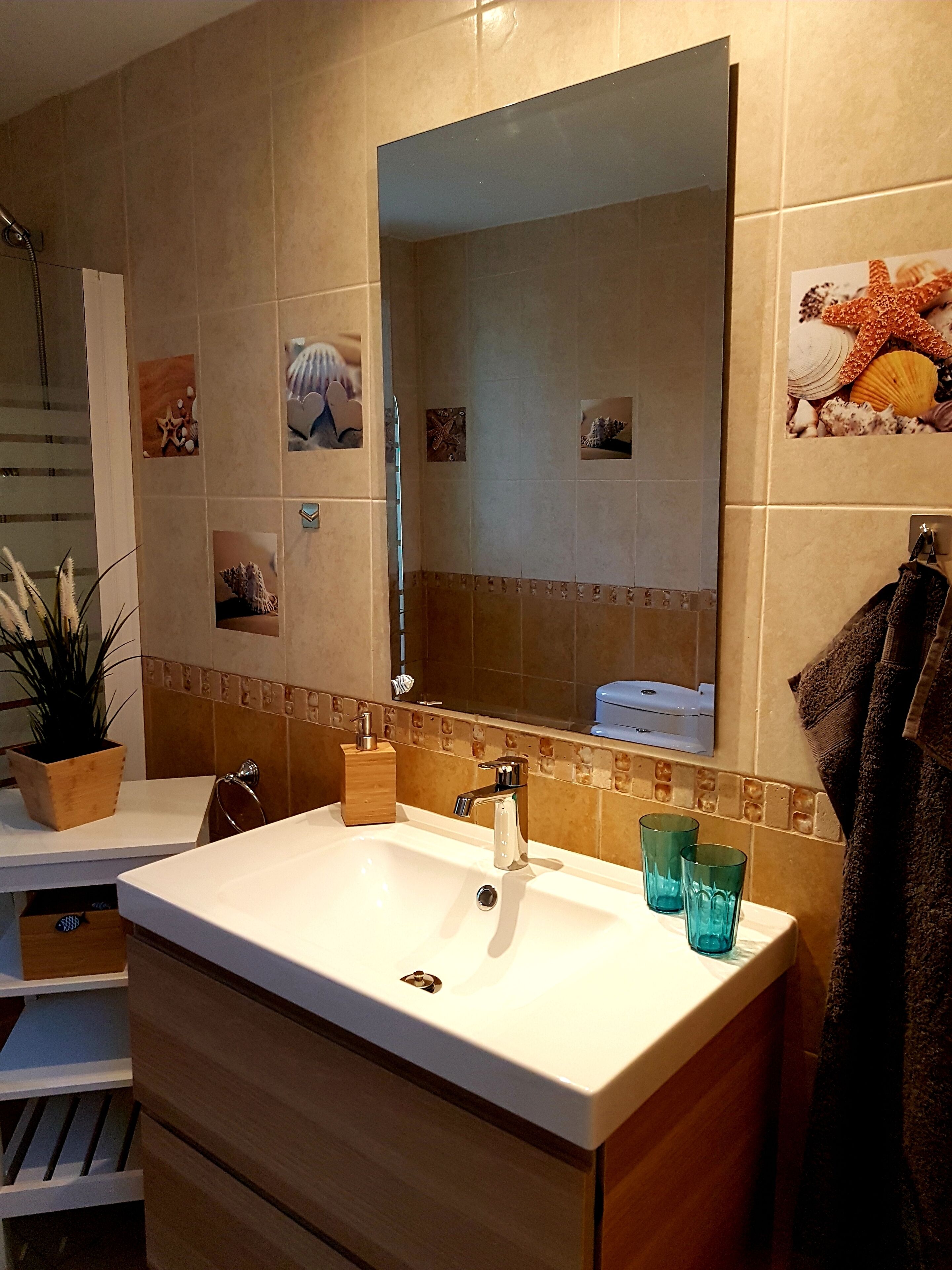 Une salle de bain avec un grand miroir, un lavabo blanc, un porte-serviettes et une plante en pot.