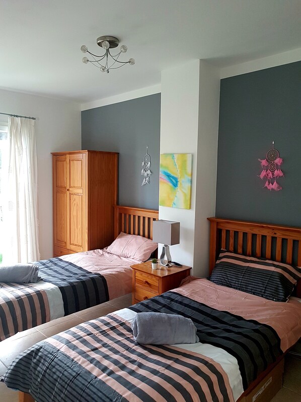 A bedroom with two beds, wooden wardrobe, bedside tables, and a ceiling light.