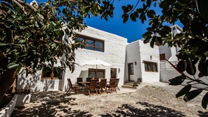 Ein weißes Gebäude mit einer Terrasse, die einen Tisch, Stühle, ein Fenster und eine Tür zeigt.