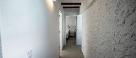 A narrow hallway with white walls and exposed wooden beams on the ceiling.