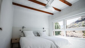 Ein Schlafzimmer mit einem großen Bett, einem Nachttisch, einem Deckenventilator und einem Fenster mit Blick auf eine felsige Landschaft.