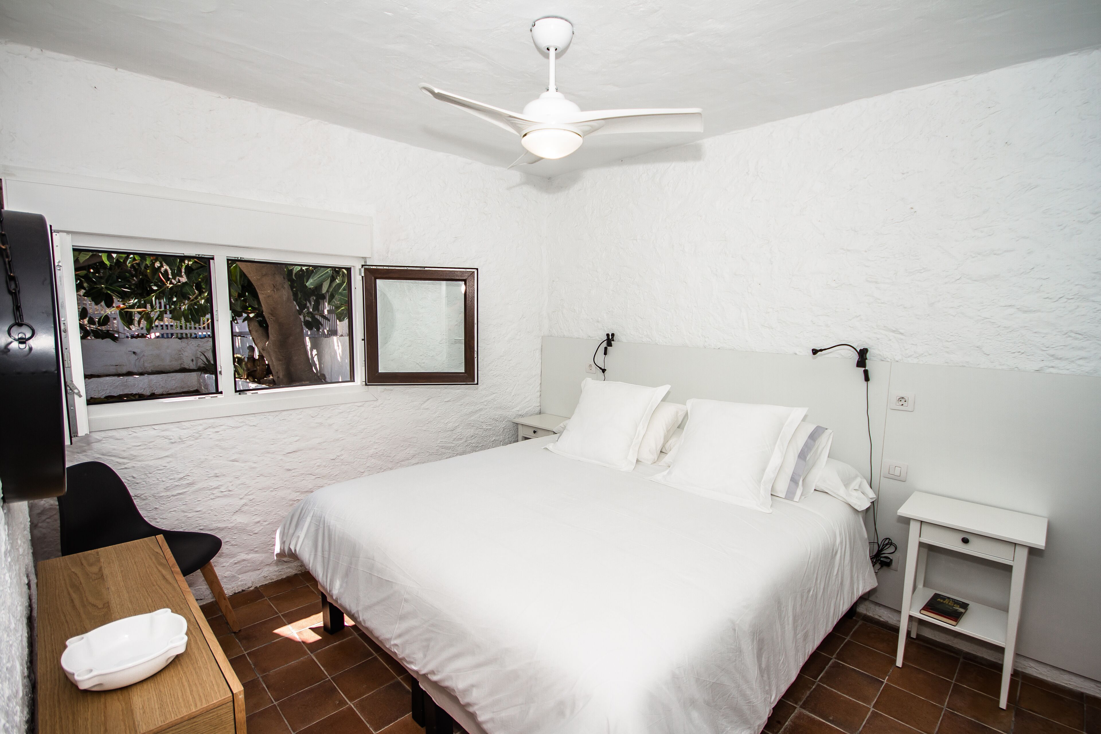 Ein Schlafzimmer mit einem Bett, einem Schreibtisch, einem Stuhl, einem Nachttisch und einem Deckenventilator.