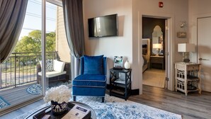 A living room with a blue chair, a flat-screen TV, a small table with a vase, and a view of the outdoors. - Downtown Exquisite Couples Weekend Getaway+Parking (Nashville)