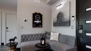 A modern living room with a grey sofa, a small round table with a candle, a decorative horse statue, a framed welcome sign, and a cityscape painting. - Downtown Exquisite Couples Weekend Getaway+Parking (Nashville)