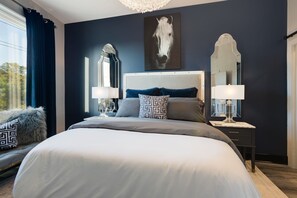 A modern bedroom with a large bed, two bedside tables with lamps, a large mirror, and a horse-themed artwork on the wall.