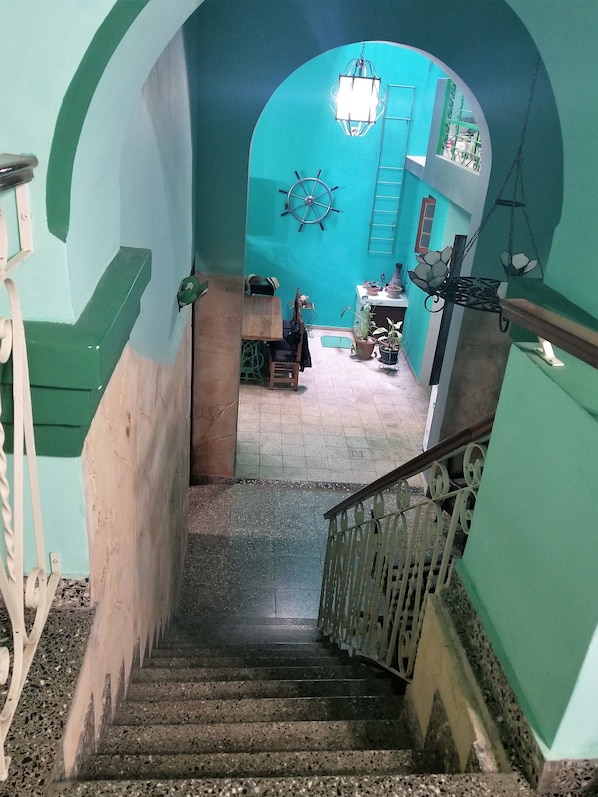 A staircase with a handrail, leading to a room with teal walls, a ship's wheel decoration, and a hanging lantern.