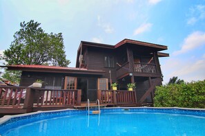 Ein zweistöckiges Holzhaus mit Balkon, Schwimmbad und Kübelpflanzen.